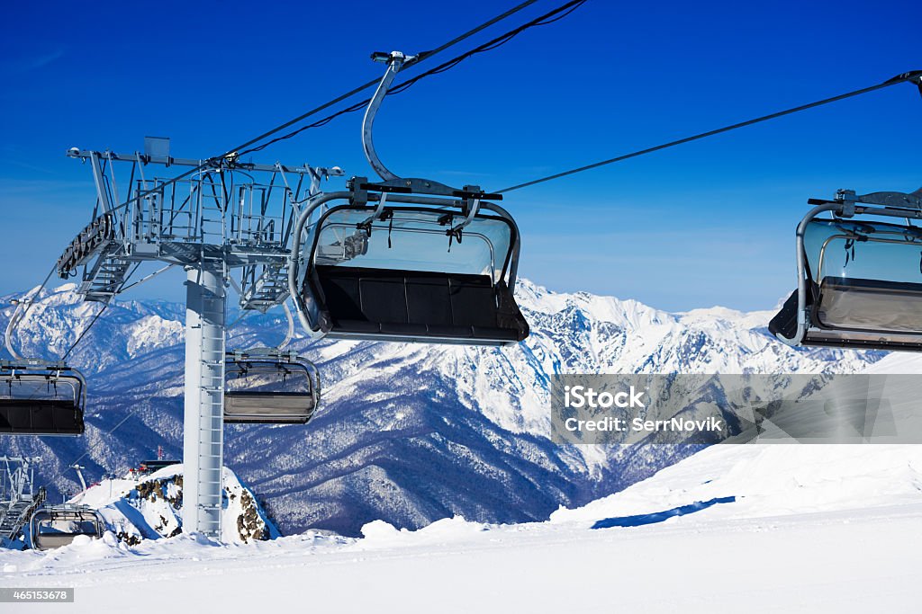 Chairs on chairlift ropeway in winter mountains View of ski lift chair on ropeway over mountains on background on winter ski resort  2015 Stock Photo