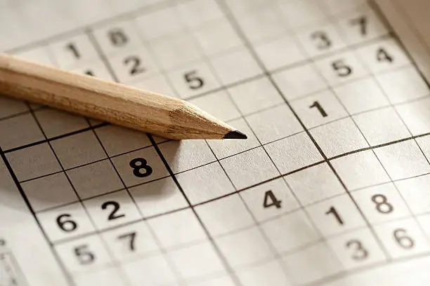 Sharpened wooden pencil lying on a sudoku grid with pre-filled numbers waiting to be completed in sequence