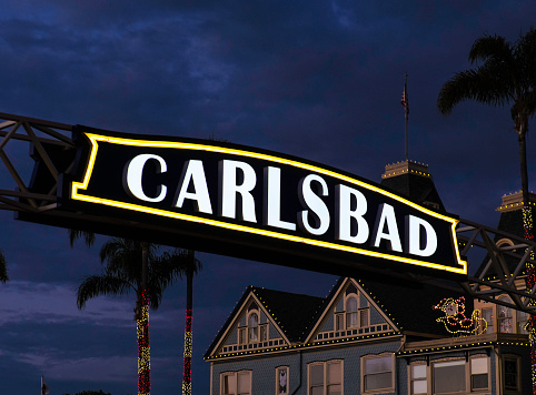 The Carlsbad Village, California Freeway Sign, at dusk, with Christmas Lights on the Palm Trees in the background.