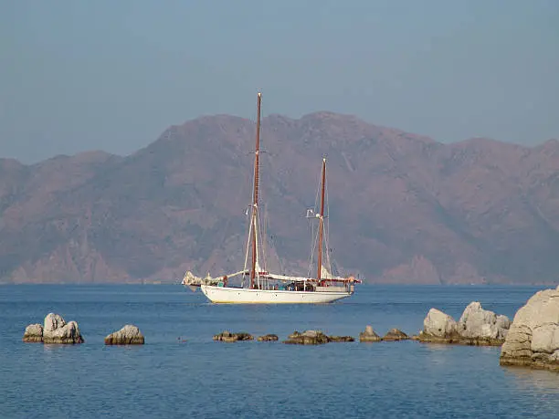 old two-master schooner is sailing in calm waters. in the background the turkish coast