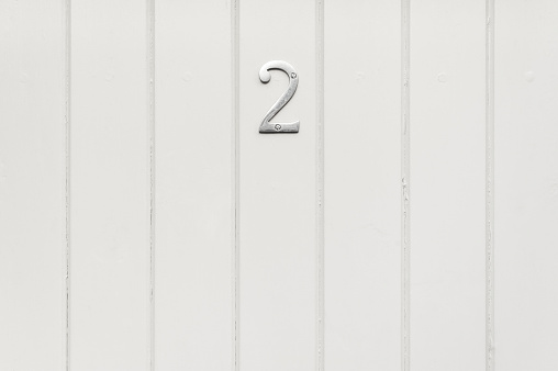 Close-up of a grey-painted wood panel door with number 2 metal sign. Soft lighting with excellent detail.