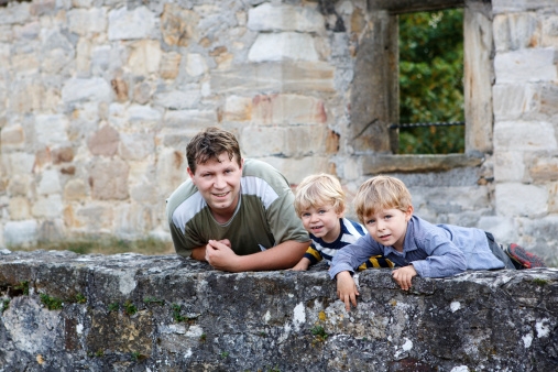 Young man and his two little boys standing behind wall of old German castle