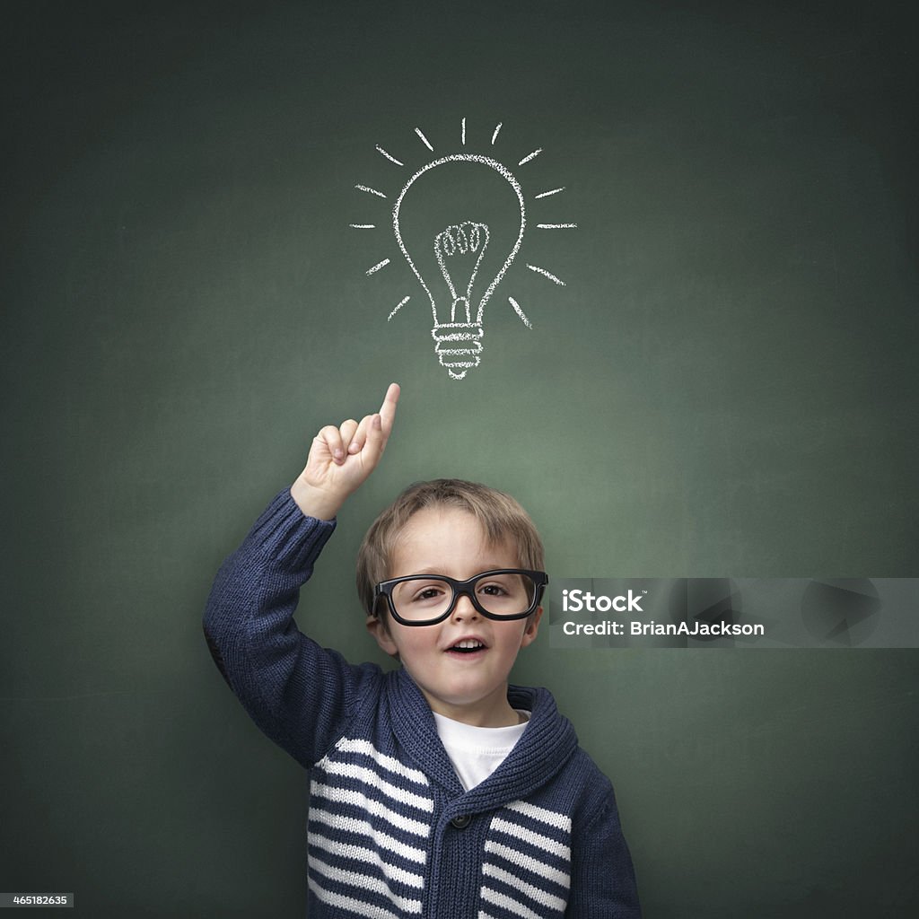 Inspirational idea Schoolboy standing in front of a blackboard with a bright idea light bulb above his head concept for innovation, imagination and inspirational ideas Child Stock Photo