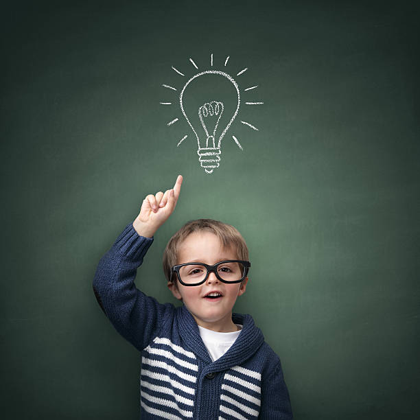 Inspirational idea Schoolboy standing in front of a blackboard with a bright idea light bulb above his head concept for innovation, imagination and inspirational ideas nerd kid stock pictures, royalty-free photos & images