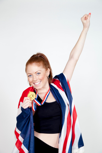 Beautiful young athletic woman celebrating with a gold medal and a large British flag.  Shot in the studio.