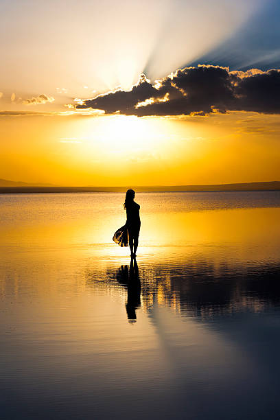 istock A women standing on a beach looking at a dreamy sunset 465200195