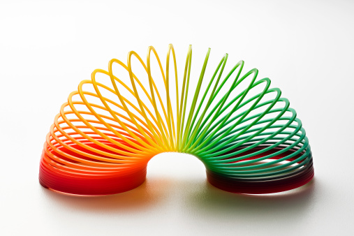 Rainbow coloured slinky toy made of a plastic wire spiral coil which enables flexibility and mobility