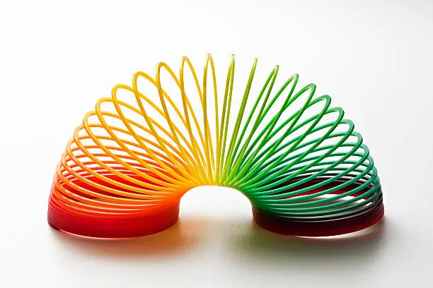 Rainbow coloured slinky toy made of a plastic wire spiral coil which enables flexibility and mobility