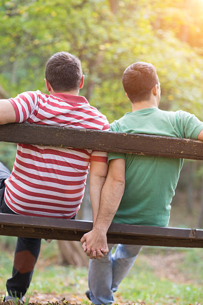 istock Two men holding hands and sitting on a park bench 465242043