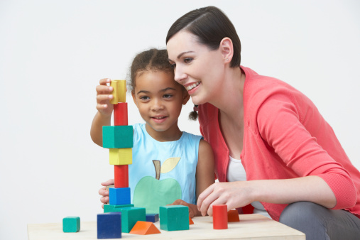 Happy Teacher And Pre-School Pupil Playing With Wooden Blocks Together