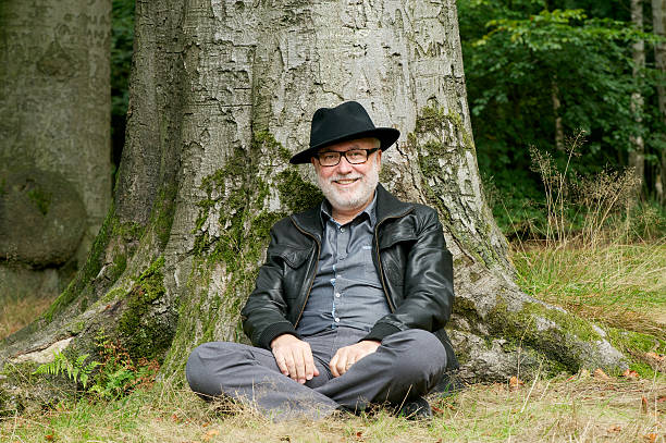 istock Happy old man sitting under tree in the forest 465249899