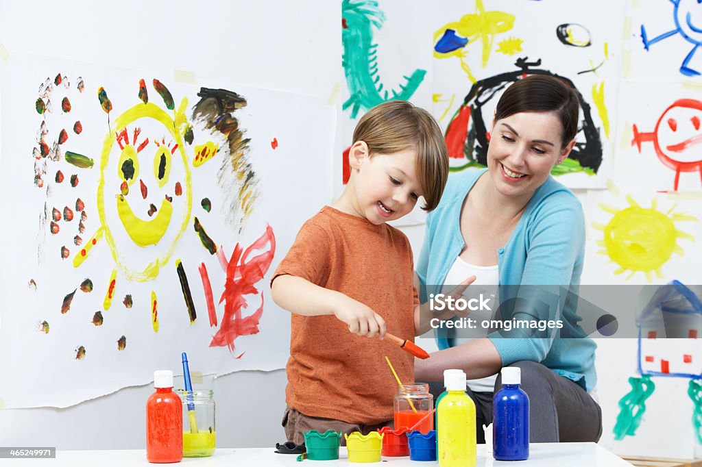 Young female teacher and pupil in pre-school art class Happy Smiling Teacher And Pupil In Pre School Art Class Painting - Activity Stock Photo