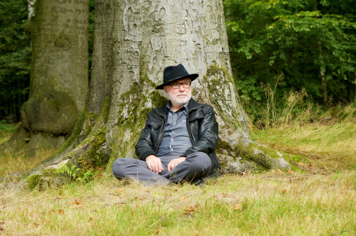 Portrait of a wise old man sitting under tree in the forest