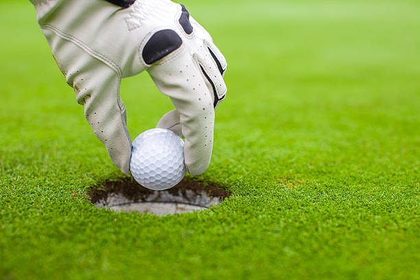 istock Man's hand putting golf ball into hole on green field 465252557