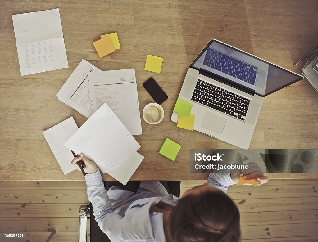 Overhead view of businesswoman working at desk Top view of young woman working at her desk with laptop and documents. Business woman working at desk in office. Brown Hair Stock Photo