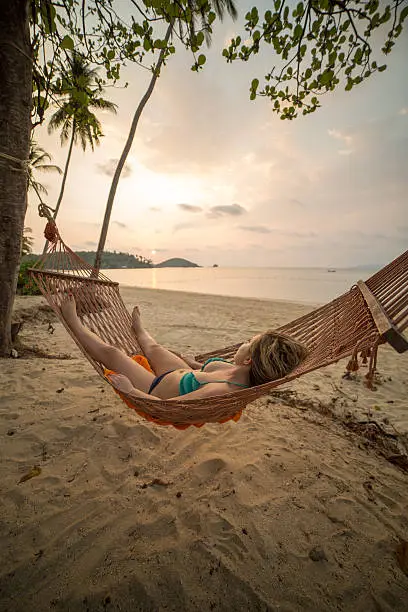 Young woman lying down on a hammock relaxing. The sun is starting to set on the beach of Koh Mak Island, Thailand.