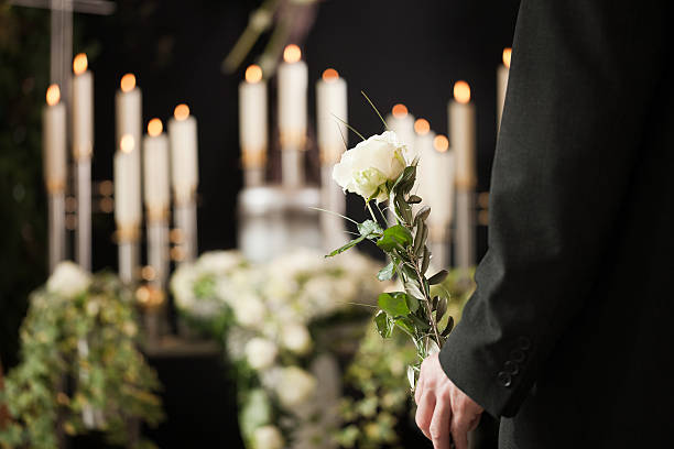 Man holding a white rose in front of urn at funeral