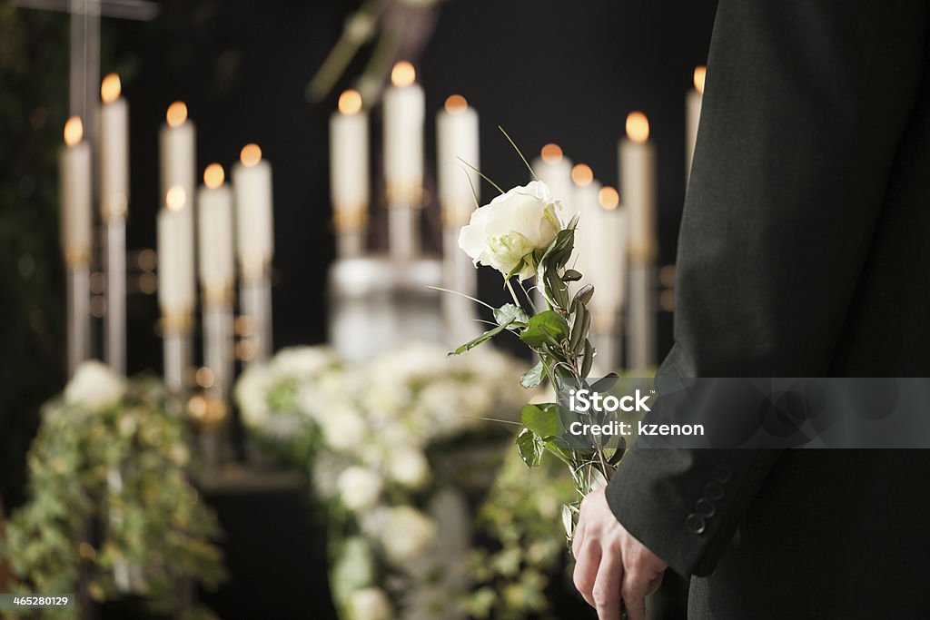 Man holding a white rose in front of urn at funeral Religion, death and dolor  - man at funeral with white rose mourning the dead Funeral Stock Photo