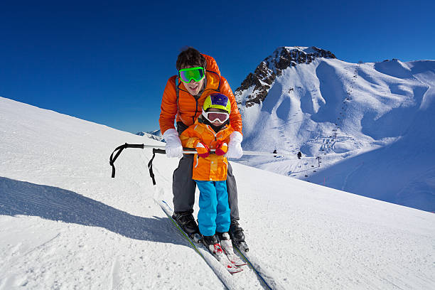Father give mountain ski lesson to little boy Little boy learns to ski on mountain resort with instructor helping to learn how to turn with mountain on background top of ski mountain stock pictures, royalty-free photos & images