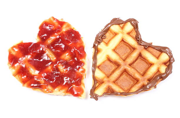 Closeup of heart shaped waffles with chocolate cream and strawberry jam. Isolated on white background
