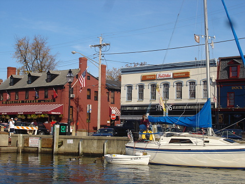 Annapolis, Maryland, USA- November 15, 2009:   Ego Alley at City Dock, Annapolis, Maryland. A sailboat with dinghy is docked along the Seawall in Ego Alley.  Tourists stroll along the Seawall.  Historic Middleton's Tavern is the visible red brick building, and other historic Dock Street Buildings are visible.  Annapolis is a historic colonial city located on the shores of the Chesapeake Bay. Annapolis is the Sailing Capital of the United States and the Capital of the State of Maryland. The city has an active waterfront for recreational boating and is a tourism destination.