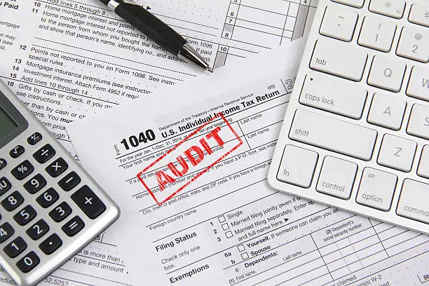 Concept image for filing federal income taxes online and being audited. Computer keyboard, calculator and pen are placed on income tax form 1040. The 'word' AUDIT is stamped on the form 1040. 