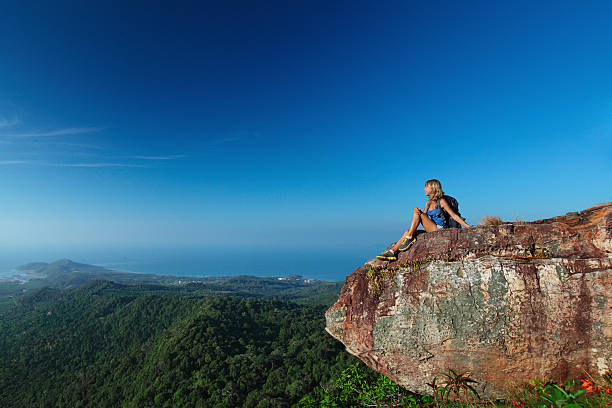 istock Female hiker sitting on clifftop looking at forest & ocean 465301694