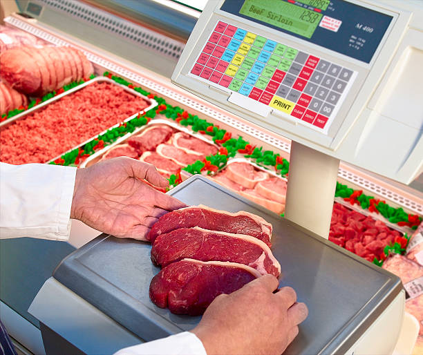 Butcher weighing beef meat steaks on scales