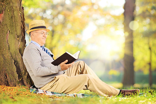 istock Senior gentleman sitting on grass and reading a novel 465309941