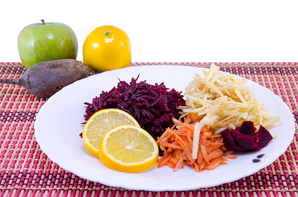 Grated carrots beet and apples with whole apples, lemon and bleet in the background