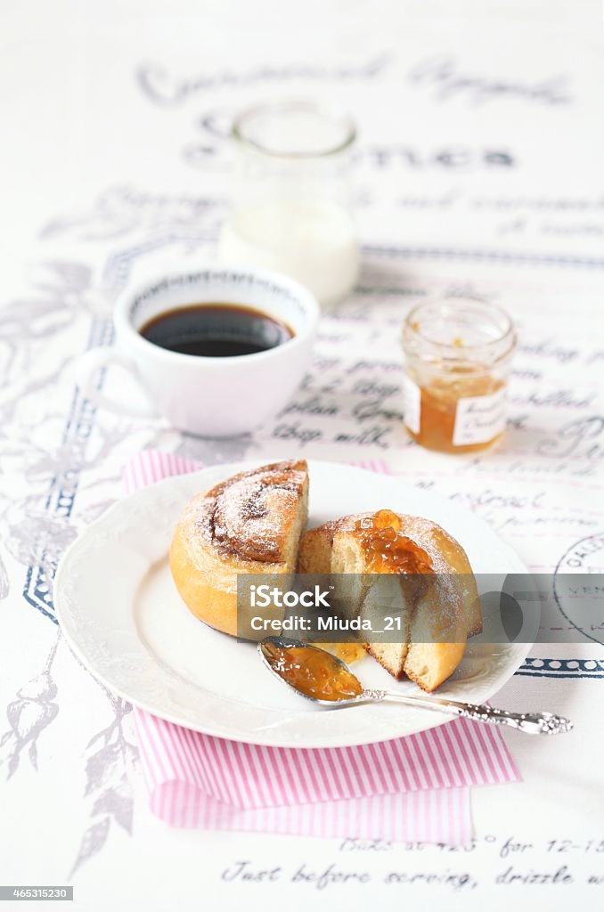 Cinnamon Roll Cinnamon Roll with orange jam on a white plate and a cup of coffee, on a light background. 2015 Stock Photo