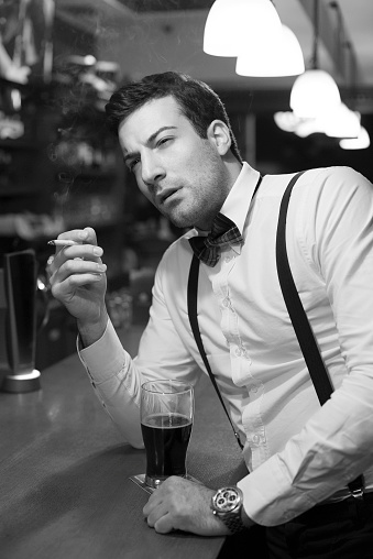 Attractive young man enjoying cigarettes and beer in the night bar