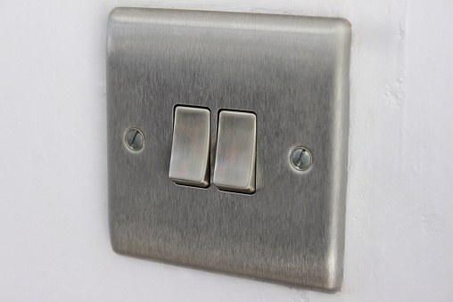 Photo showing a modern, light switch made from brushed stainless steel, that is square in shape with rounded edges.  The panel features two switches, so that different lights in the same room can be operated independently.