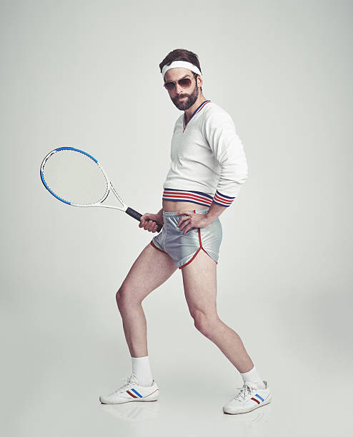 Let's hit the court! A young man in the studio wearing ill-fitting retro tennis wear and shades while holding a racquet sweat band stock pictures, royalty-free photos & images