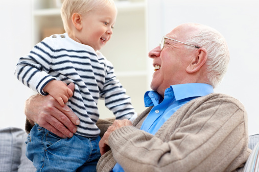 Happy senior man with his grandson sitting on sofa smiling at each other - Indoors