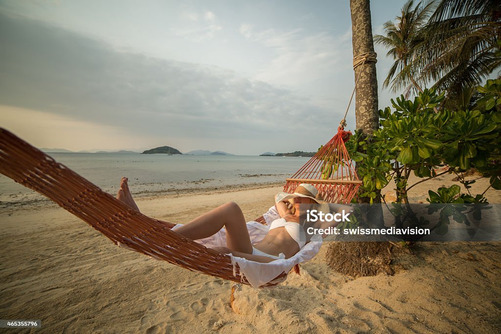 Young woman on beach lying down on hammock Young woman on a tropical beach in Thailand lying down on a hammock relaxing. Sunset time on the Island. Shot with 5D Mark III. 2015 Stock Photo