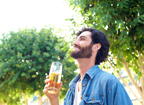 Portrait of a young man laughing with a glass of beer at an outdoor bar in summer