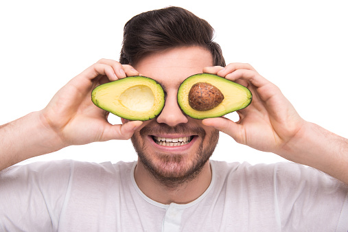 Young man is holding avocado in front of his eyes isolated on white background.Man is holding avocado, isolated on white background.