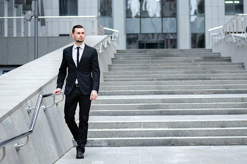 Confident businessman coming down the stairs. Young man in a suit is going to work