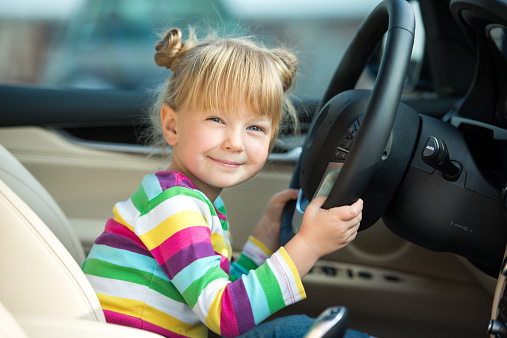Cute little girl sitting inside car and pretending to drive it. Concept for car rental