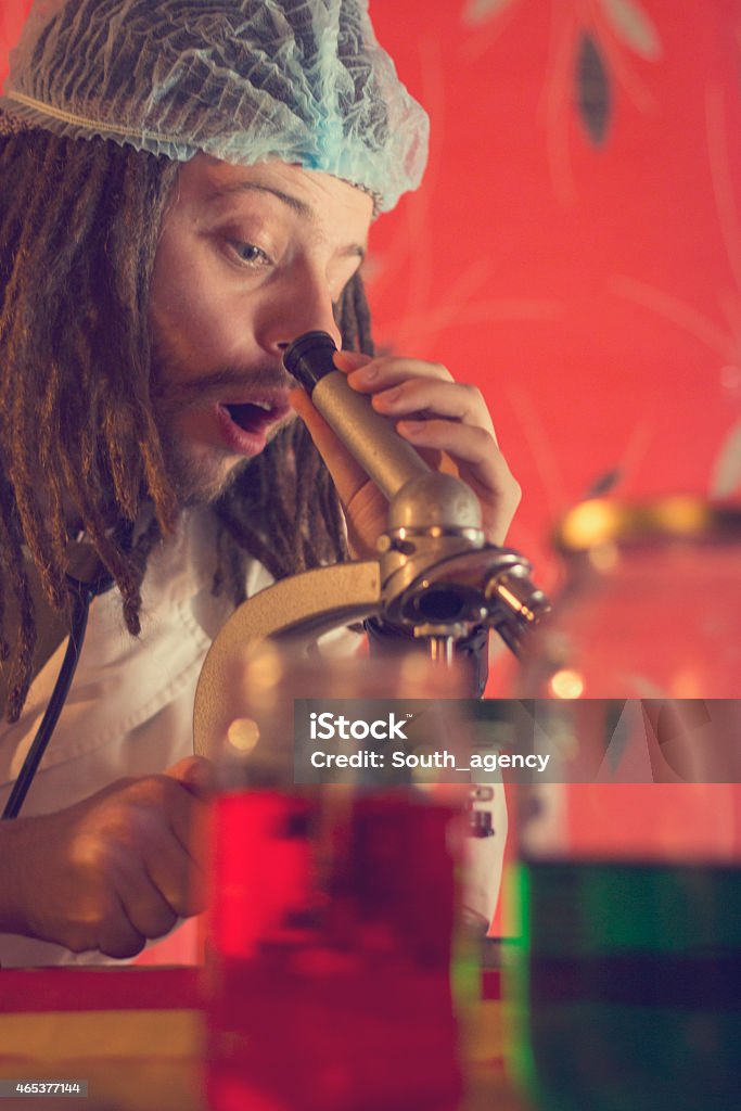 Mad professor with dreadlocks looking through a microscope Mad scientist in his lab 2015 Stock Photo