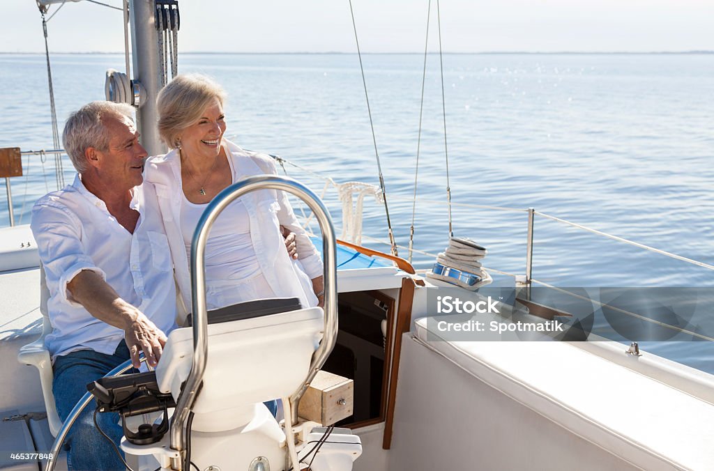 Happy Senior Couple Sailing Yacht or Sail Boat A happy senior couple sailing and sitting at the wheel of a sail boat on a calm blue sea Senior Adult Stock Photo