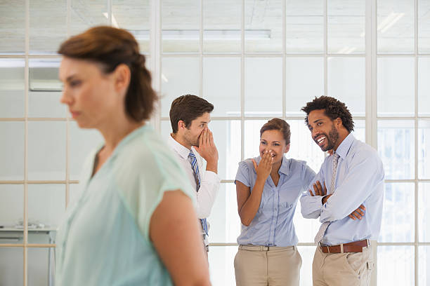 Colleagues gossiping with sad businesswoman in foreground stock photo