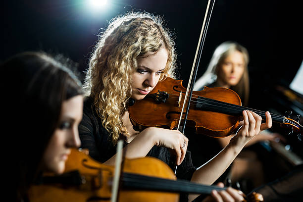 Trio female orchestra. Three women playing musical instruments. Focus is on the middle, on young woman playing violin. string instrument stock pictures, royalty-free photos & images