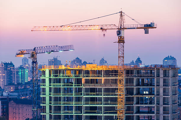 costruzione di edifici di uffici su viola tramonto con due gru - skyscraper nobody steel construction foto e immagini stock