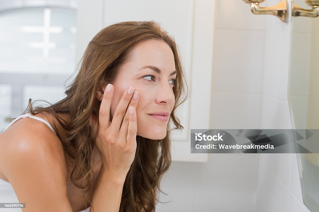 Side view of a beautiful young woman examining her face Side view of a beautiful young woman examining her face in the bathroom at home Women Stock Photo