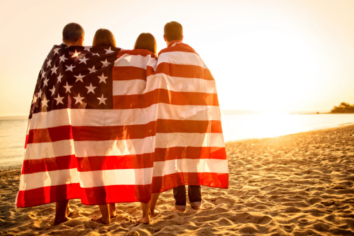 Four people wrapped in the United States Flag embracing each other