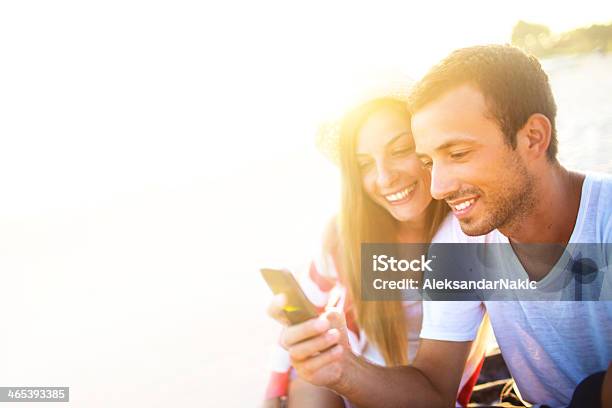 Couple Using A Smart Phone On The Beach Stock Photo - Download Image Now - Portable Information Device, 20-29 Years, Adult