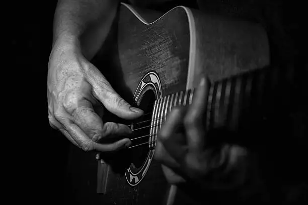 Black and white Picture . Close up of a guitarplayer . The Hand of the player looking aged. High contrast.