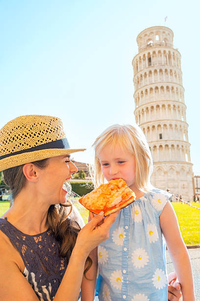 Mother and baby girl eating pizza near tower of pisa Happy mother and baby girl eating pizza in front of leaning tower of pisa, tuscany, italy pisa leaning tower of pisa tower famous place stock pictures, royalty-free photos & images
